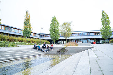 Studierende sitzen am Eingangsbereich zur Hochschule