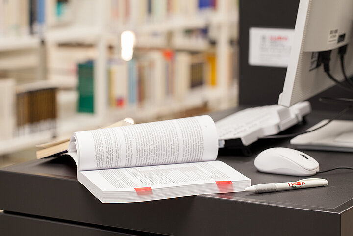 Lernplatz Hochschule Buch auf Tisch neben PC